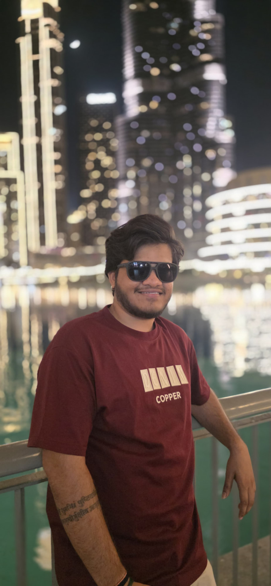 Portrait of Meet Rafaliya standing by a railing with illuminated Dubai towers behind him