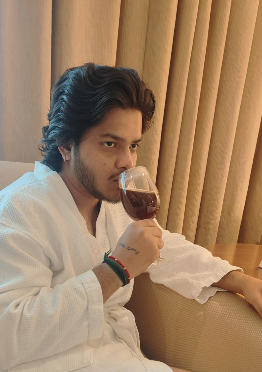 Relaxed portrait of Meet Rafaliya in a white robe enjoying coffee by warm curtains